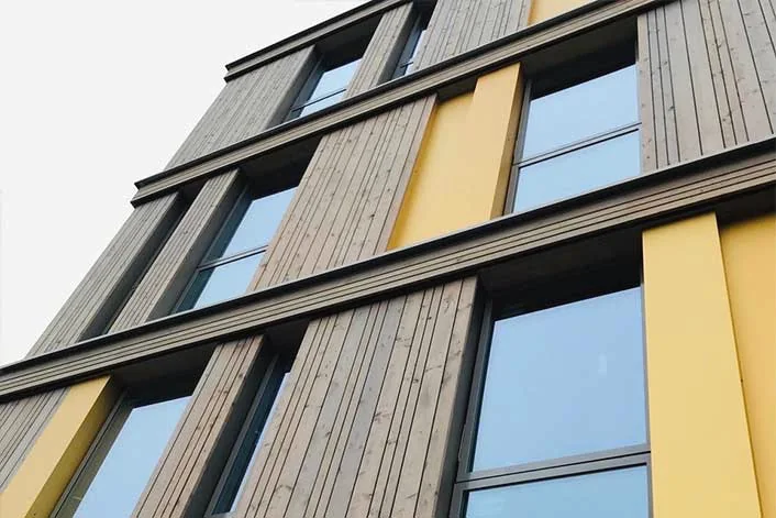 Fassade mit Holz und gelben Paneelen